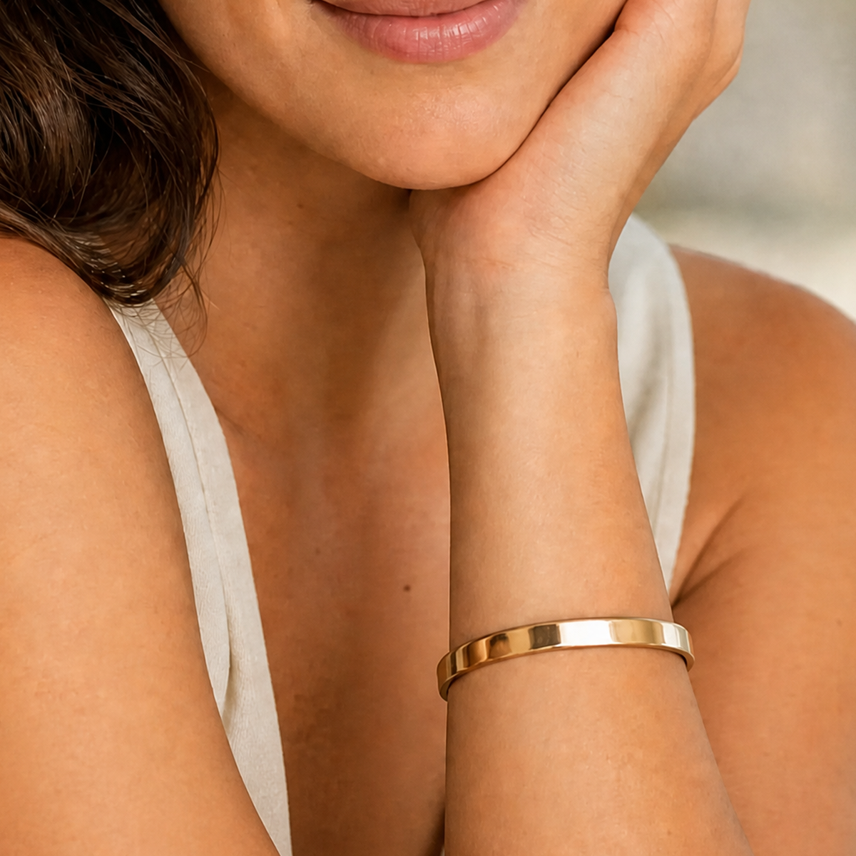 Gold-tone HEMATIX cuff worn on a woman’s wrist with an ivory outfit